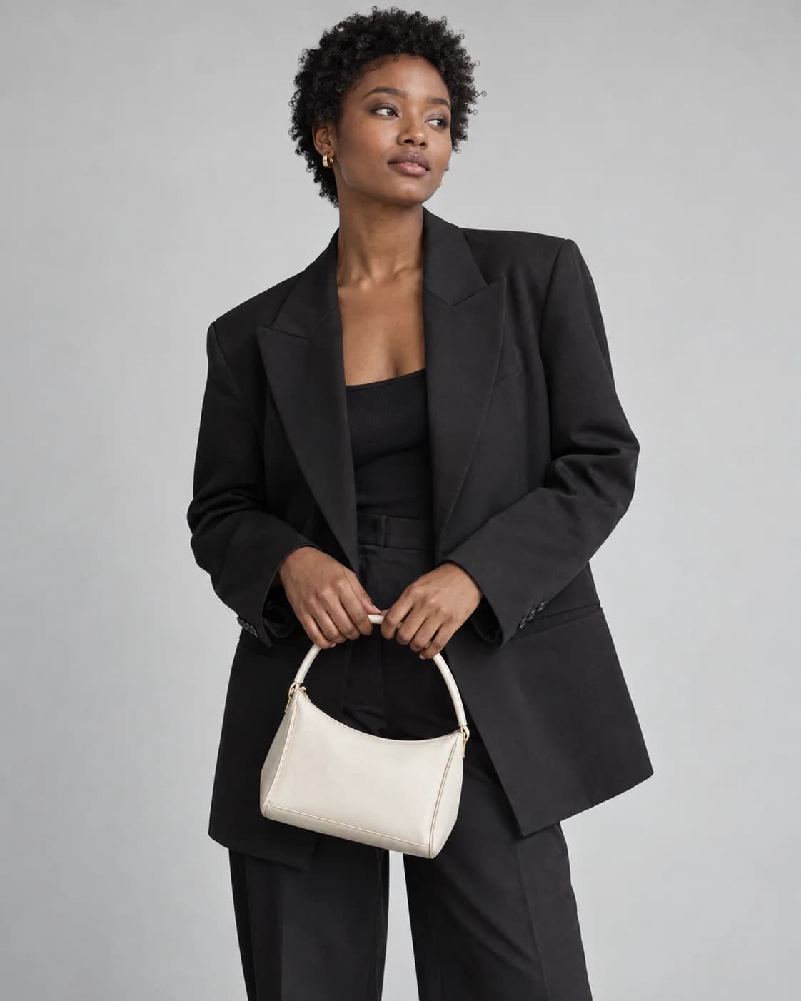 Adult fashion model in a black blazer holding an ivory handbag