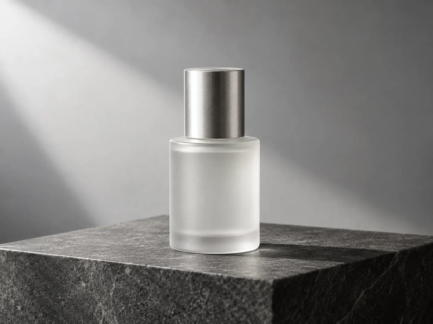 Frosted serum bottle with a silver cap on a charcoal stone plinth in soft studio light